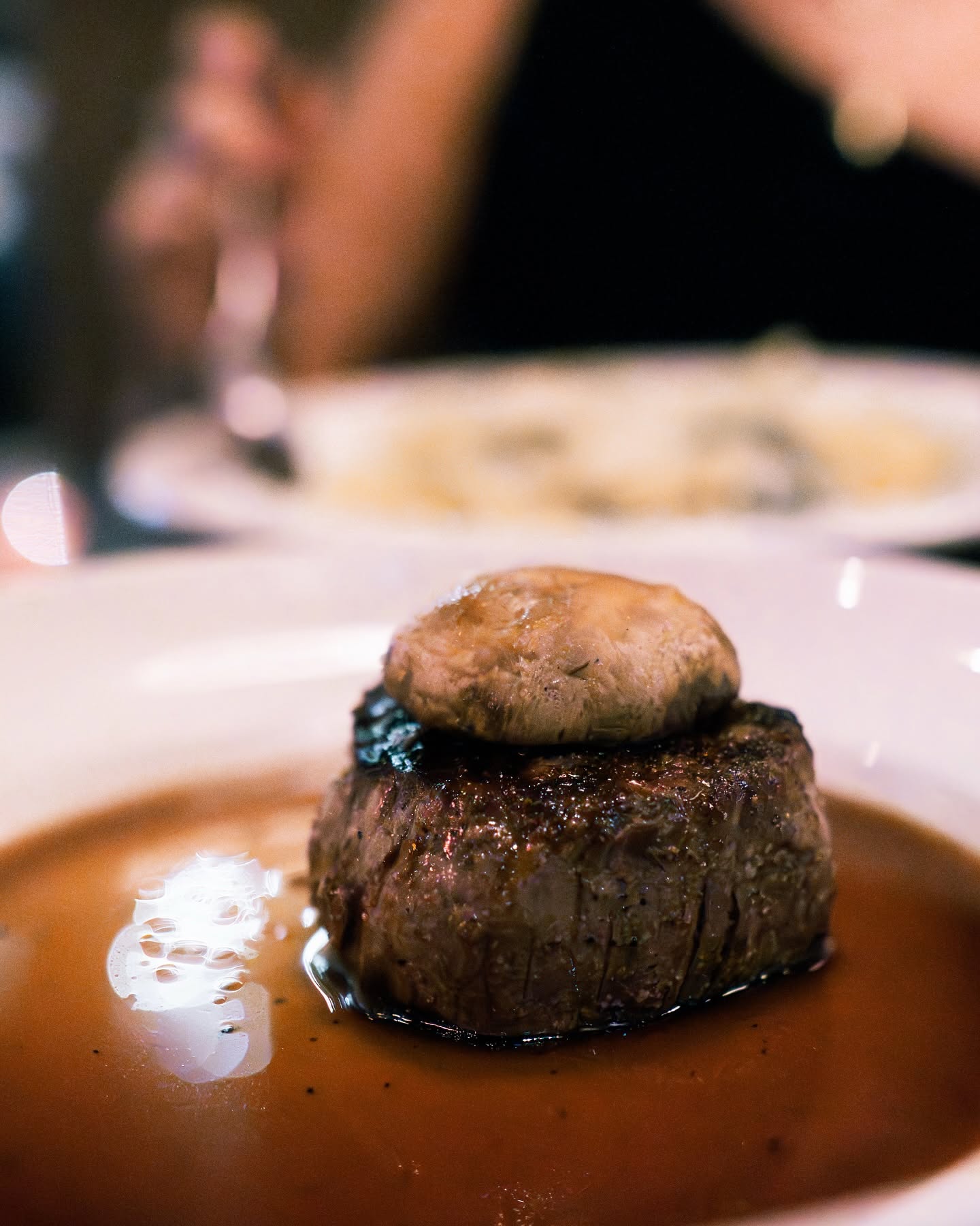 A thick, seared filet mignon topped with a roasted mushroom cap in a pool of jus.
