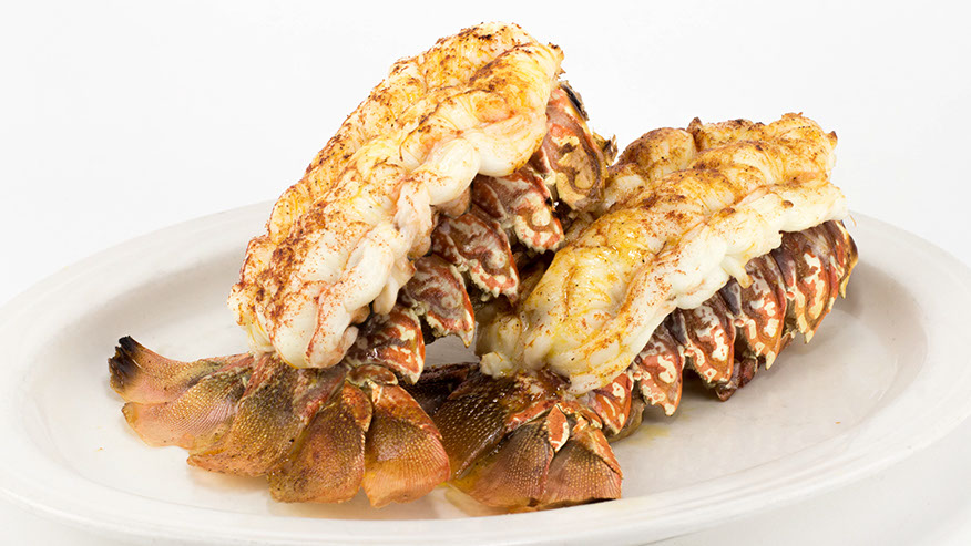 Two broiled lobster tails on a white plate.